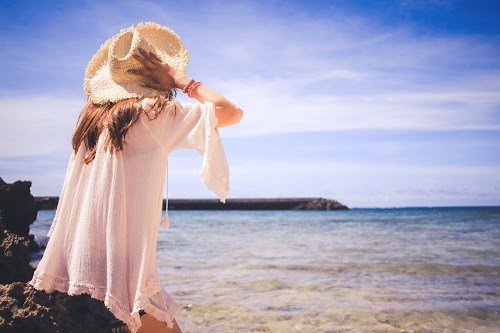 フリー写真画像『海で風に飛ばされそうな帽子をギュッと押さえて座っている女の子』[ID:6528]