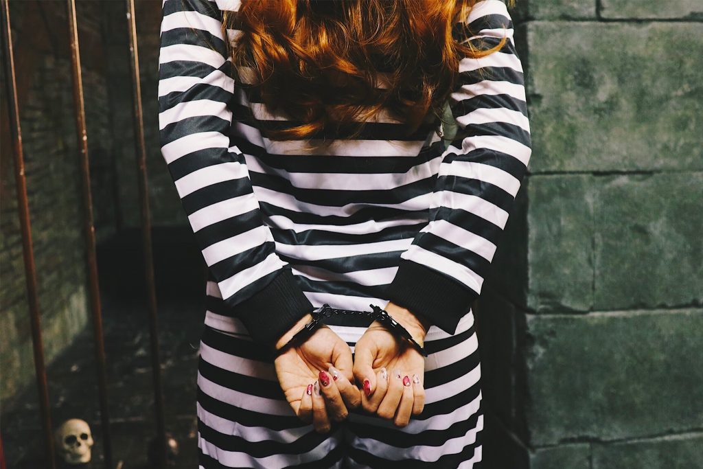 フリー写真画像『手錠をかけられ牢屋の前に立たされる囚人の女の子』[ID:9172]