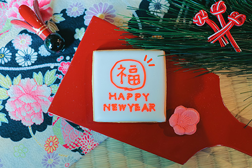 フリー写真画像『【年賀状画像】羽子板に乗った『HAPPY NEWYEAR』のアイシングクッキー（黒和柄背景）』[ID:10870]