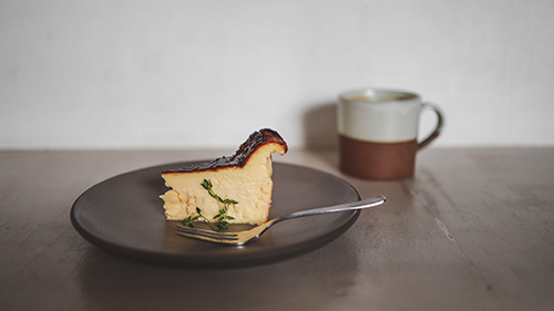 フリー写真画像『バスクチーズケーキとホットドリンクが置いてあるカフェのテーブル』[ID:15515]