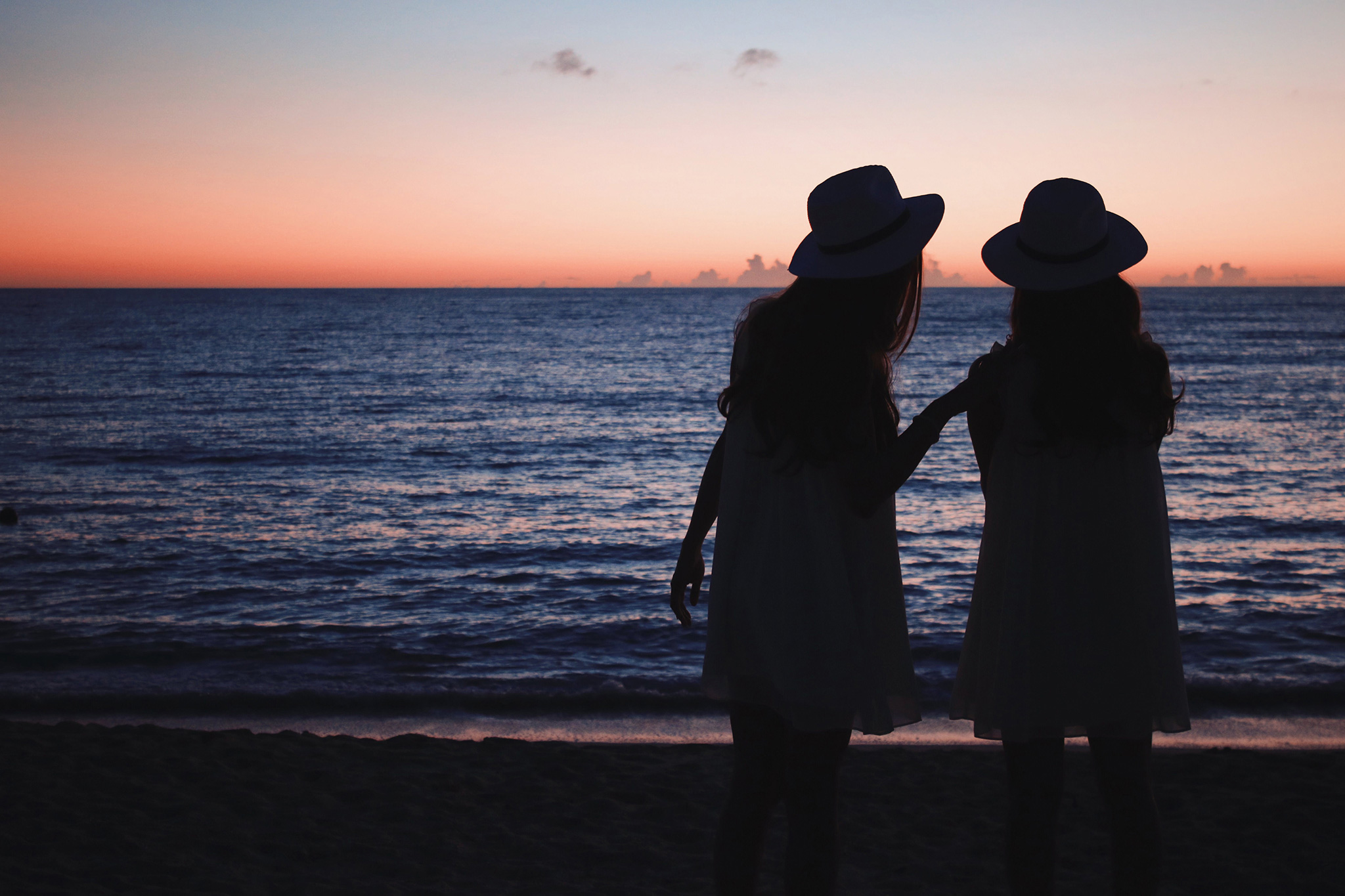 夕日が沈む海を見ながらおしゃべりしている双子の女の子たちのフリー画像｜おしゃれなフリー写真素材：GIRLY DROP